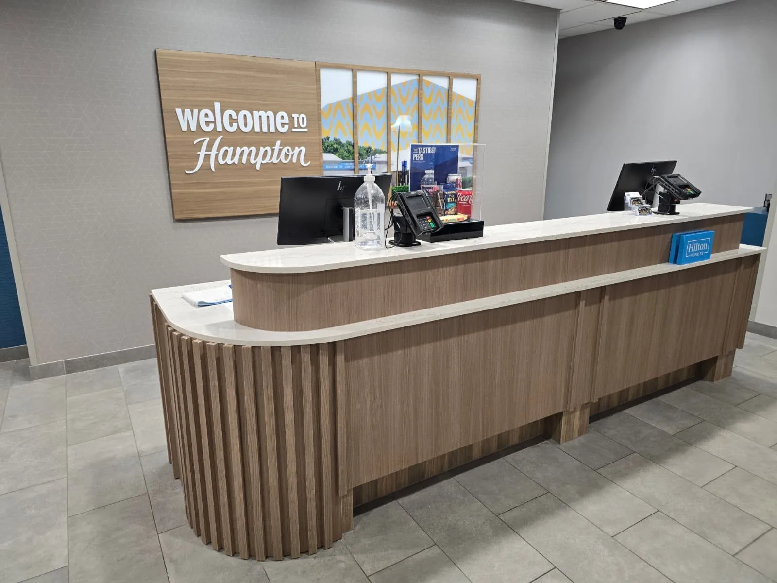 Reception desk with a rounded slatted end, wood-toned front panels, and light-colored counter surfaces.