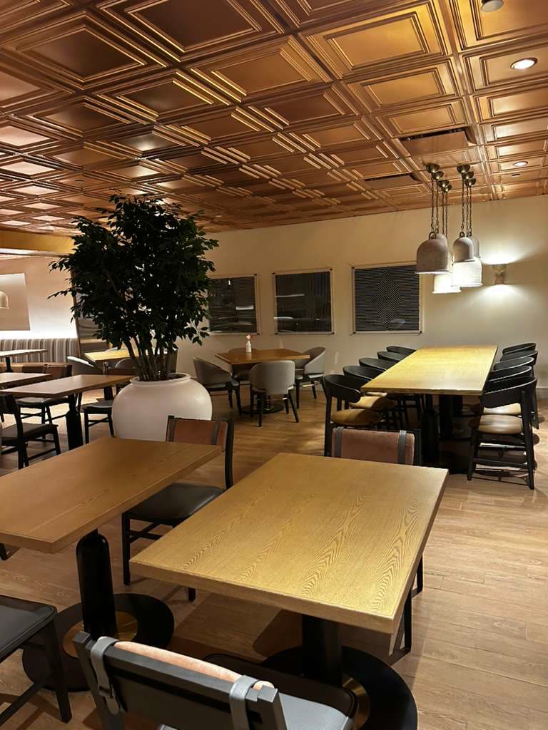 Coffered ceiling above dining tables, banquette seating, and a long communal table with pendant lights.